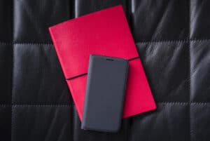 A mobile phone sits on a pink notebook which sits on a leather banquette