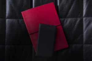 A mobile phone sits on a pink notebook which sits on a leather banquette